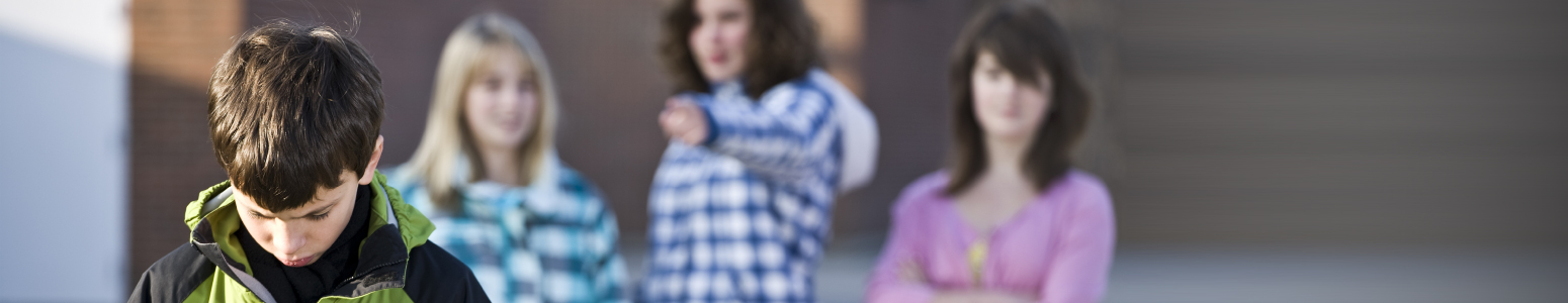 Three girls bully a boy at school, one of the girls is pointing at him