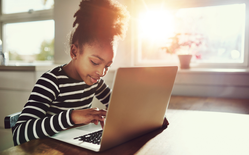 Student sitting at a table while happily working on laptop