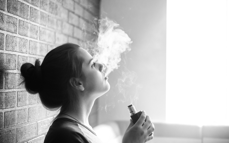 Student vaping against a brick wall